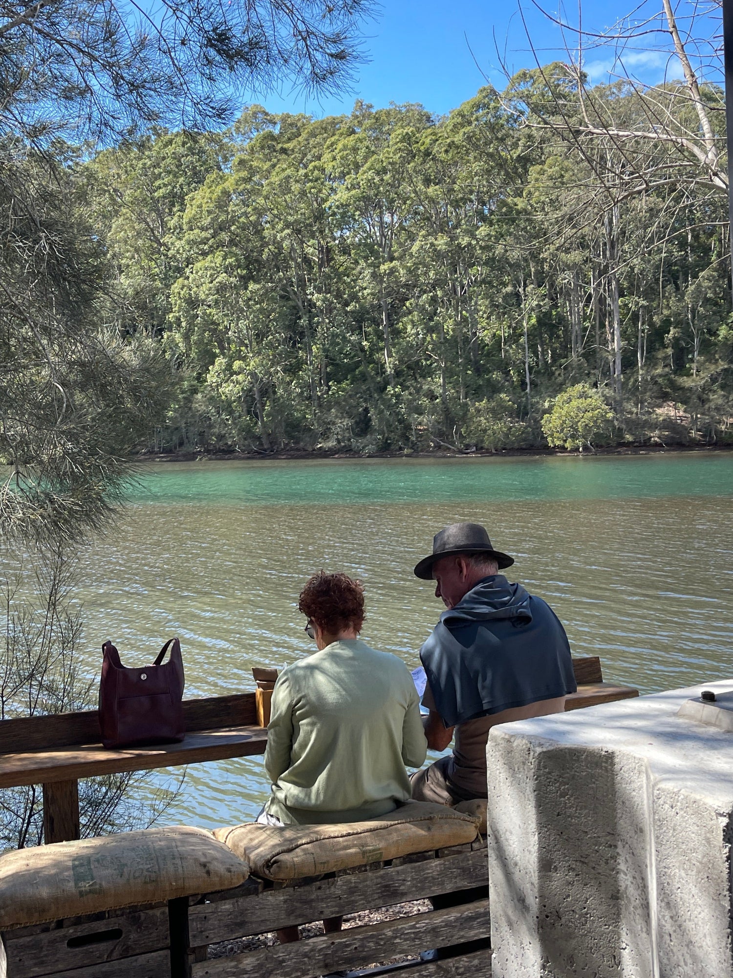 Two people sitting at a wooden table by a lake with trees in the background