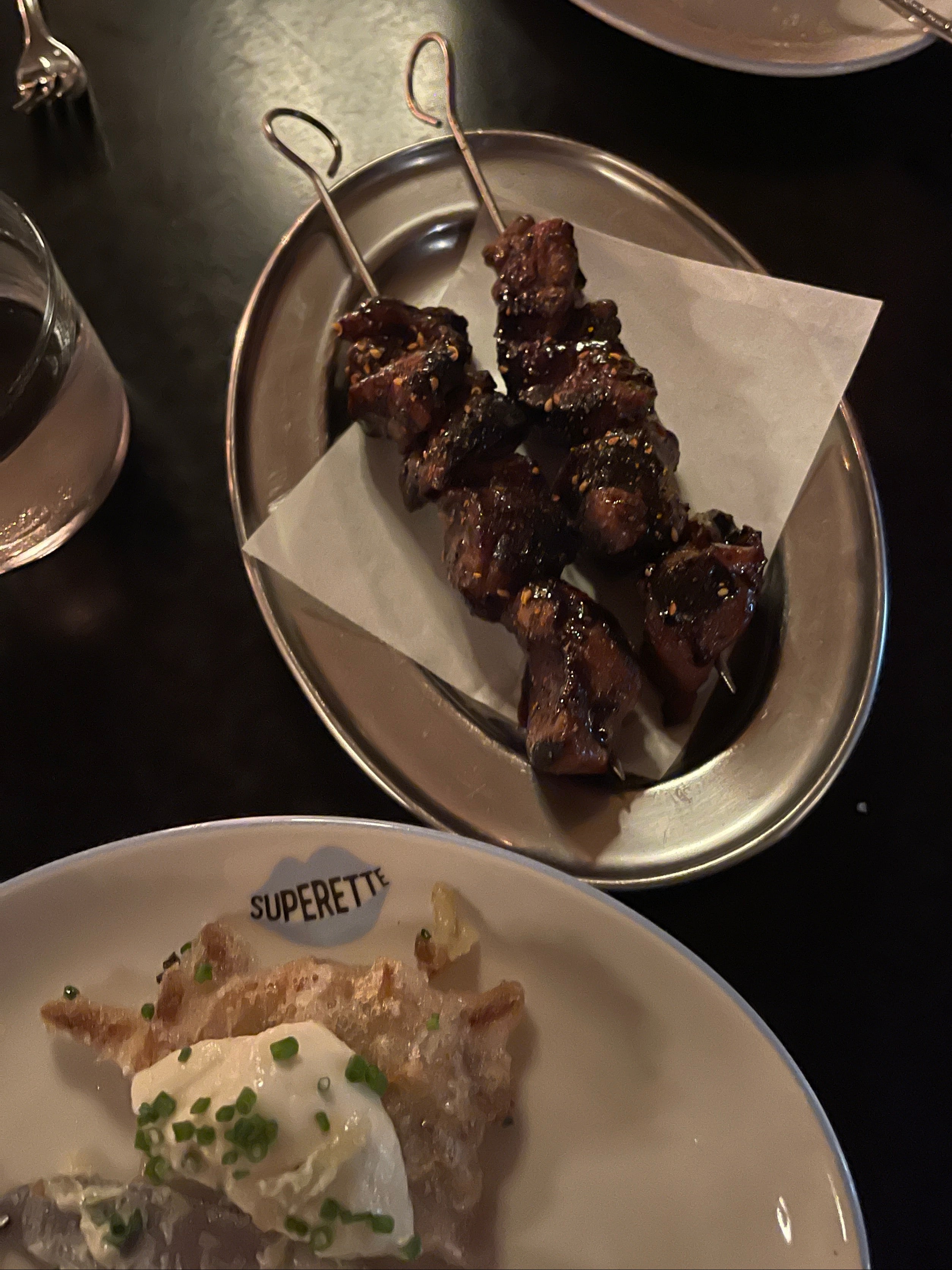 Skewers of food on a metal plate with a side dish on a dark surface